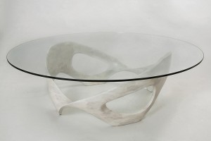 This photo shows an organic, sculpted wood coffee table base made of bleached cherry wood with a half-inch, circular glass top