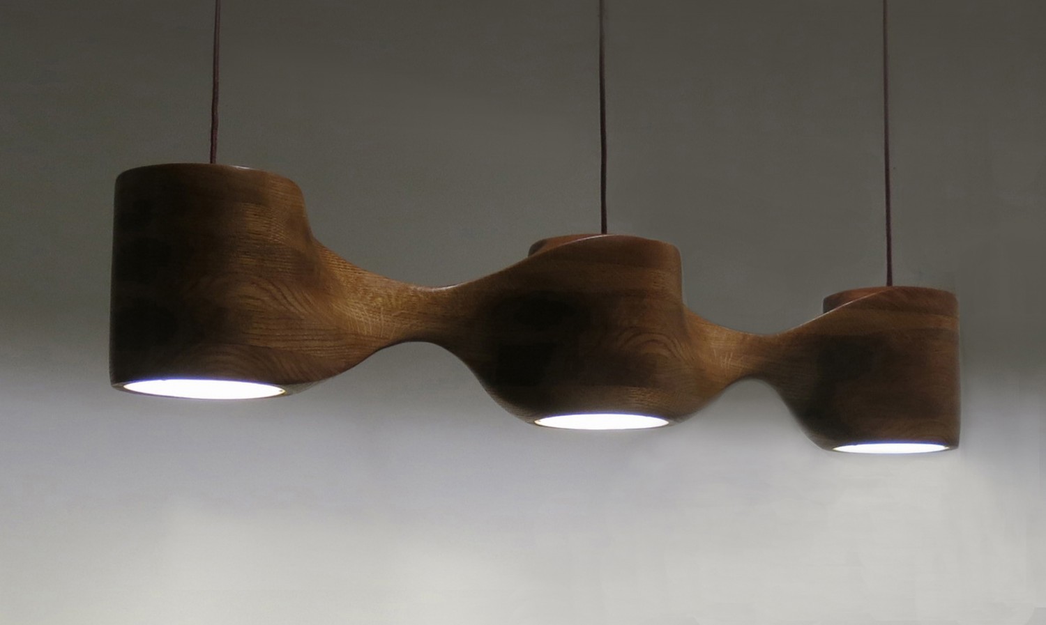 This photo shows a pendant light with three lamps made from oak, seen from three-quarters view