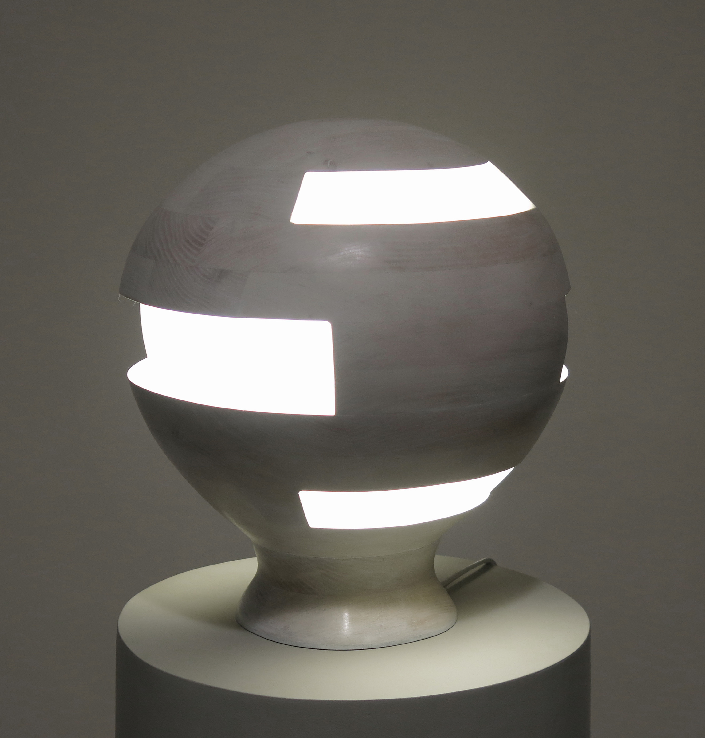 This photo shows a spherical lamp made of wood with irregular cutouts for the light to pass through